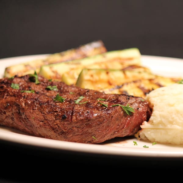 Grilled steak with parsley, mashed potatoes, and grilled zucchini on a white plate.