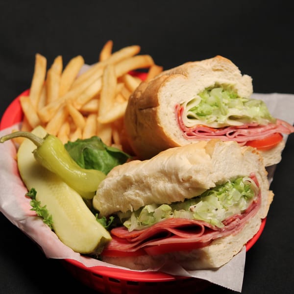 Italian sub sandwich with fries, pickle spear, and pepperoncini in a red basket.
